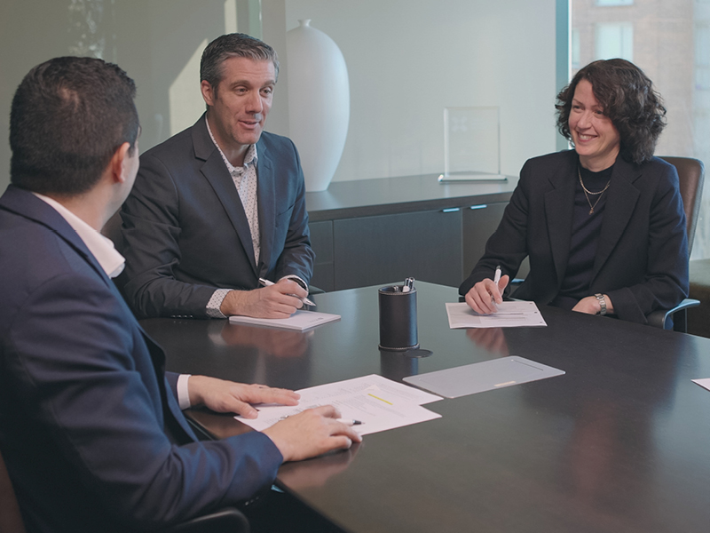 : Two businessmen and a businesswoman sit at a conference table.||||