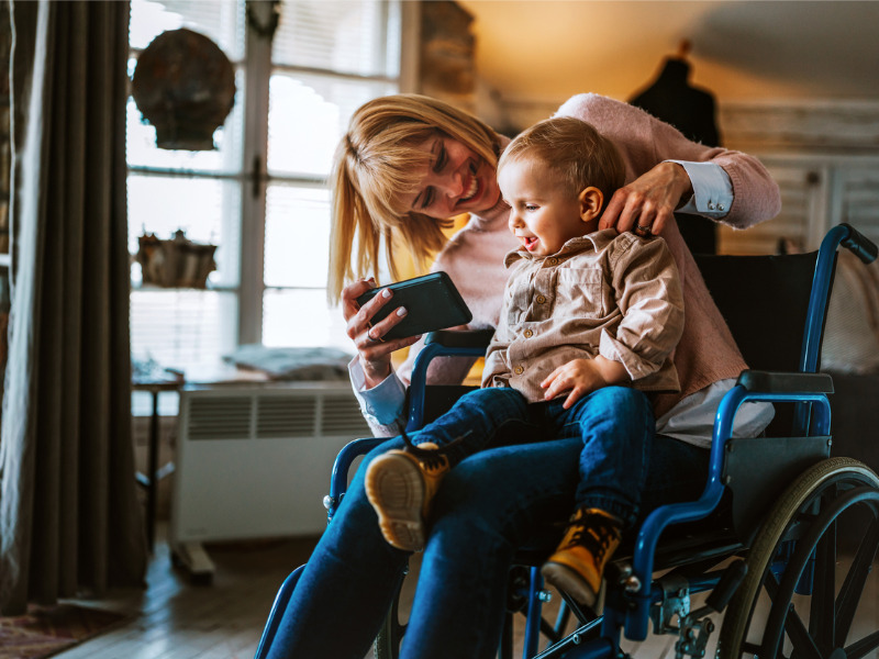 Happy smiling mother with disability in wheelchair playing with child at home|