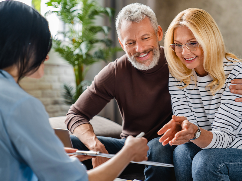 Financial advisor showing terms of contract to happy couple on notepad