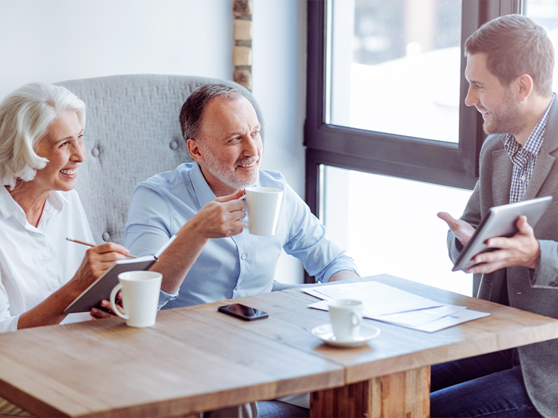 Aged couple drinking coffee meeting with sales manager around a kitchen table