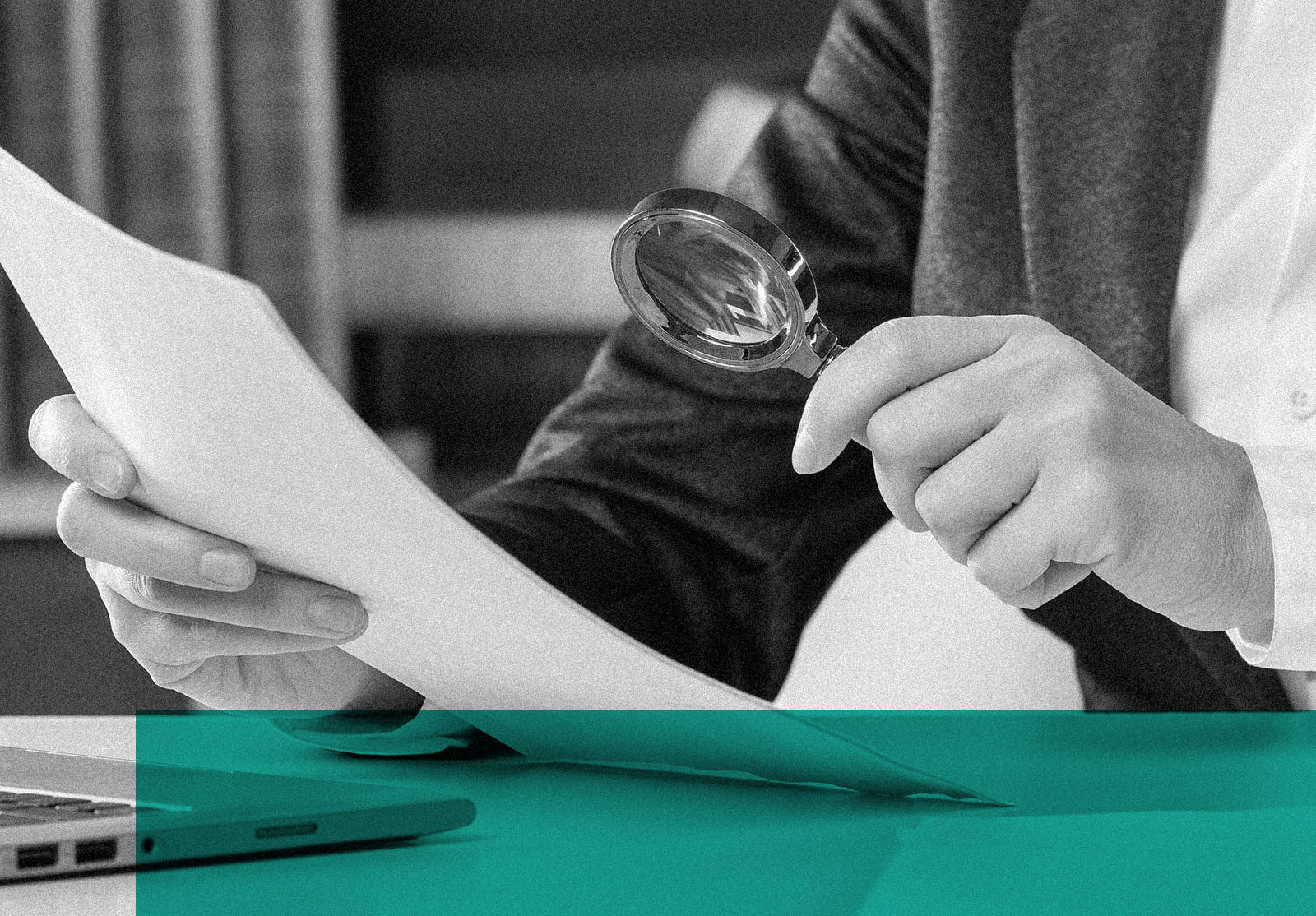 Female hands with a golden loupe and a papers at the desktop next to open laptop